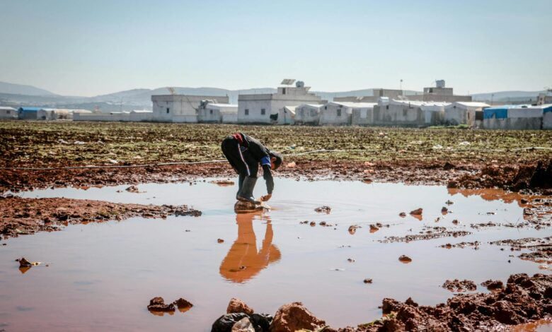 Full body of anonymous male pouring dirty water on legs in pond surrounded with settlement of refugee